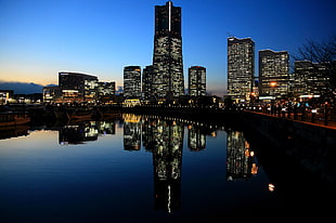 high rise buildings with lights turned on near body of water HD wallpaper